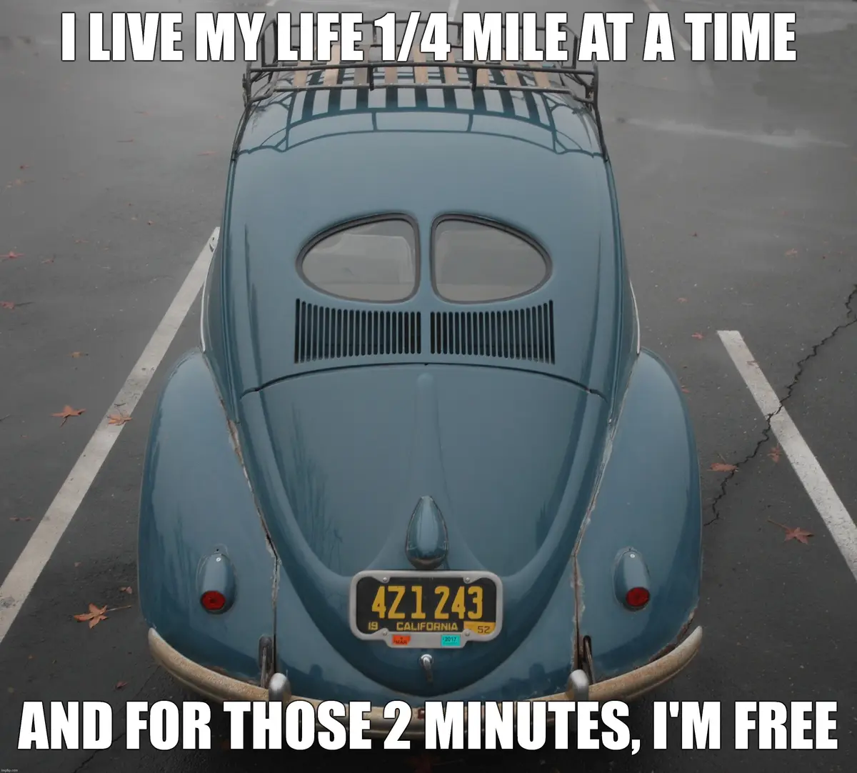The image shows the rear view of a vintage blue Volkswagen Beetle parked in a parking space, with white lines marking the…