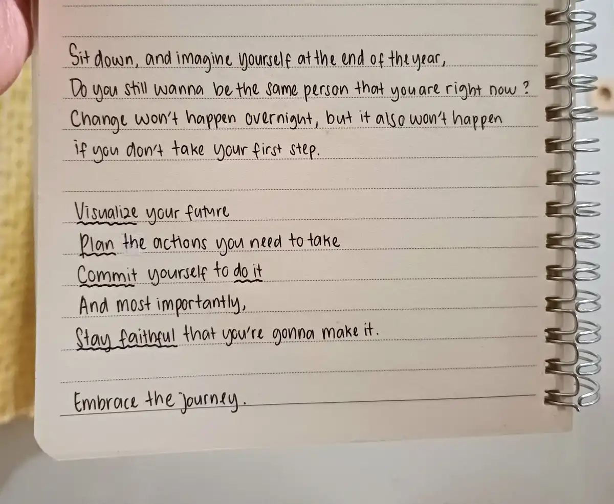 A close-up photo of a spiral-bound notebook with handwritten motivational text in black ink on lined paper. The text…