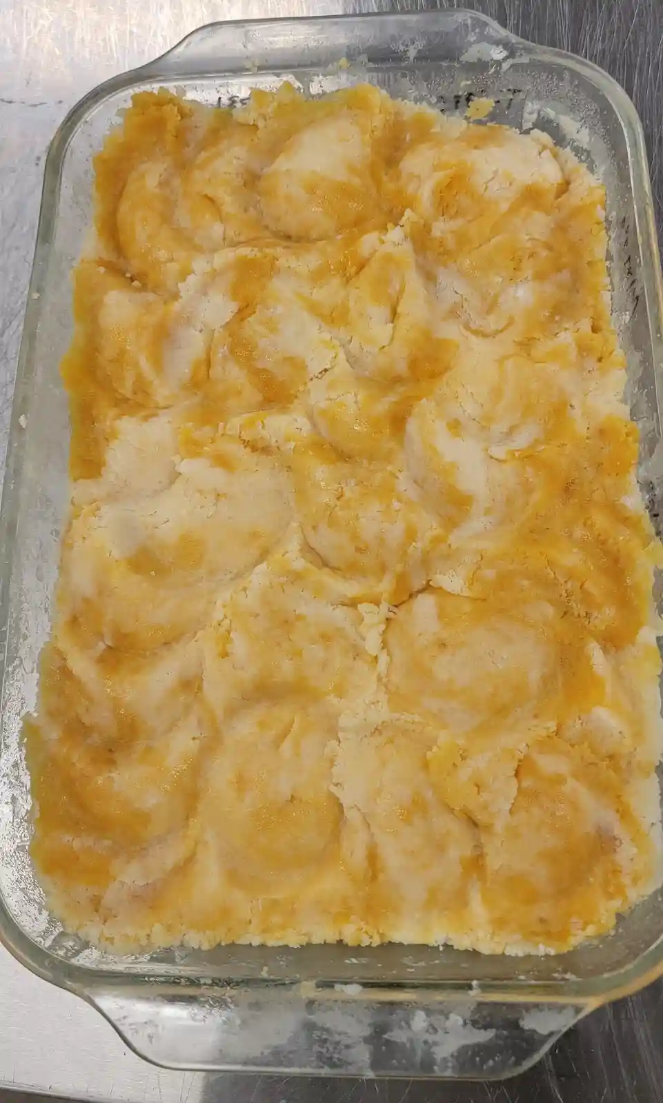 A glass baking dish contains a lumpy, uneven mixture of yellow and white batter, resembling poorly mixed cake batter or a…