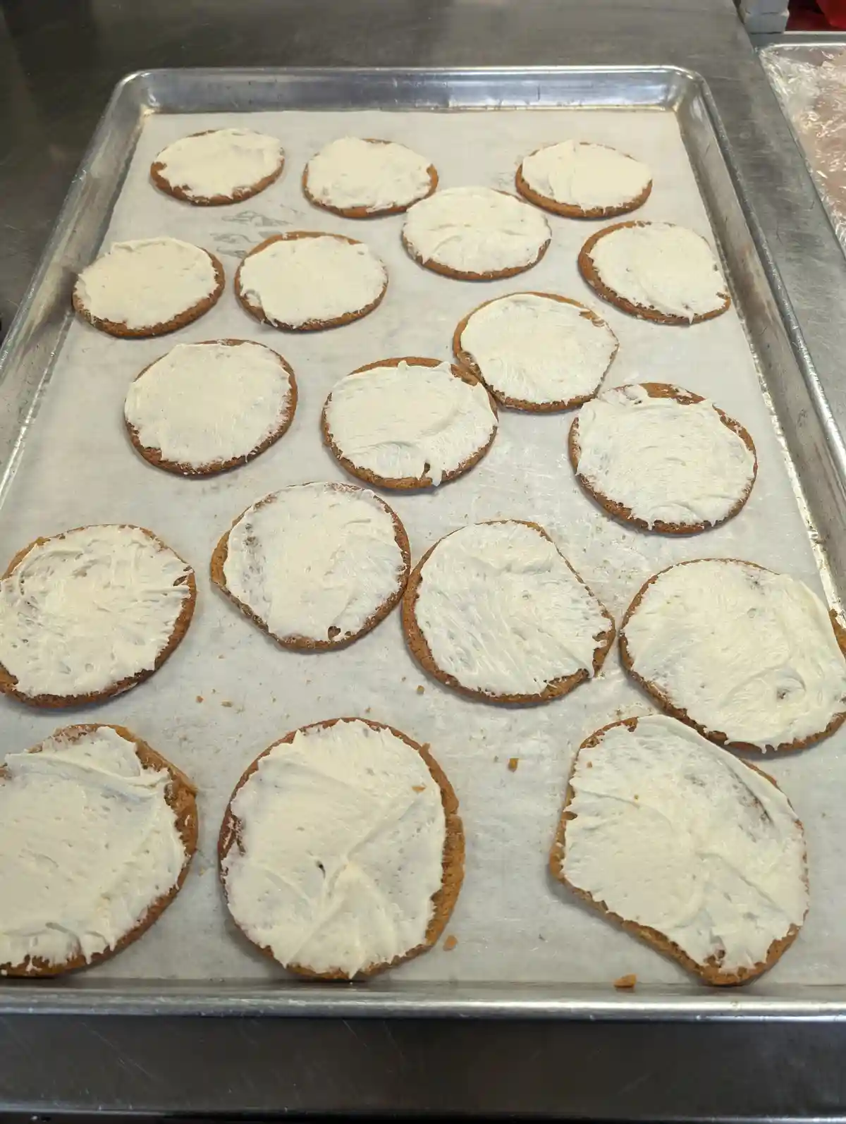 A metal baking tray lined with parchment paper holds numerous round, golden-brown cookies, each generously covered with…