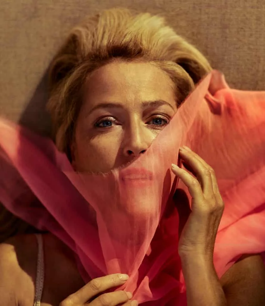 a woman with blonde hair and blue eyes lies down, holding a sheer pink fabric over her face, revealing only her eyes and…