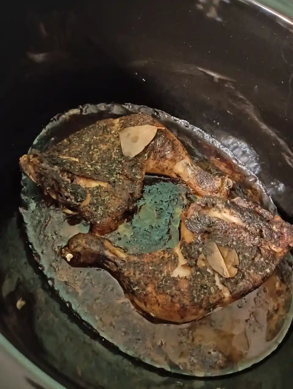 A close-up photo shows four heavily seasoned, darkly roasted chicken legs in a black pot, partially submerged in dark liquid…