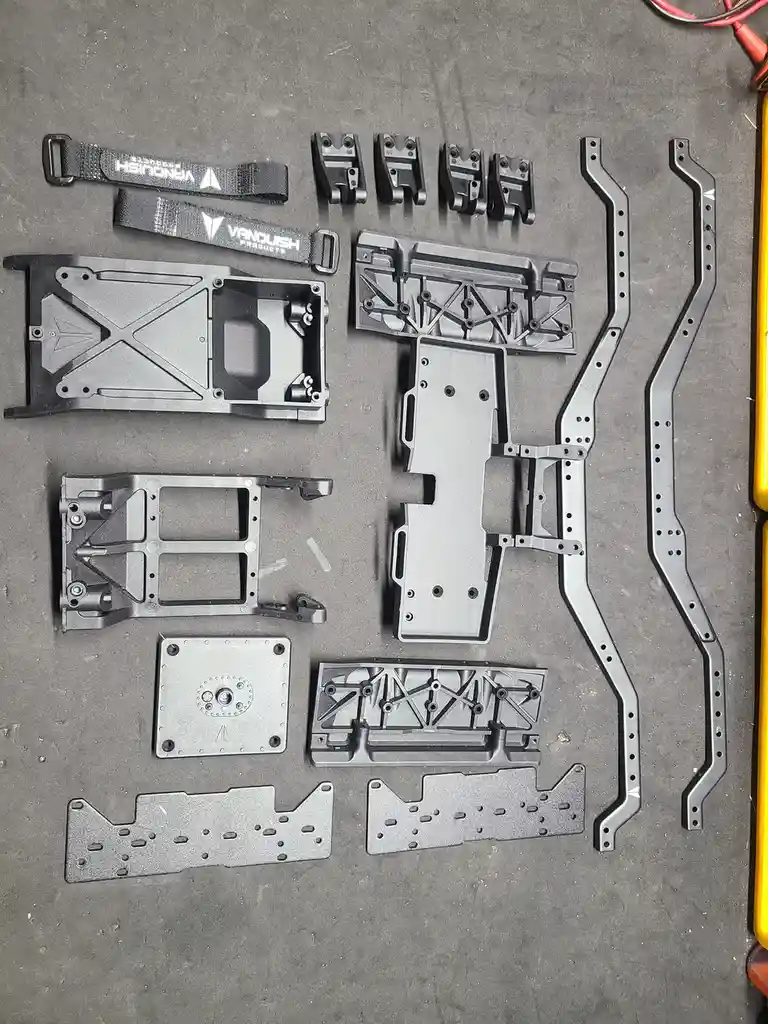 An overhead shot displays numerous disassembled metal components, including brackets, plates, and two branded wrist straps…