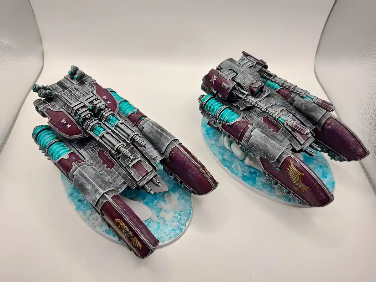 Two intricately painted miniature warships, likely from the Warhammer 40,000 universe, sit side-by-side on circular bases…