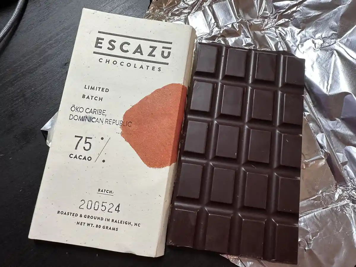 A bar of Escazu Chocolates, labeled as 75% cacao, is shown next to its wrapper on crumpled foil. The wrapper details include…