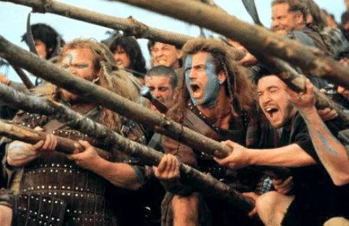 A group of warriors from the movie 'Gladiator' are shown in a tense battle scene, gripping wooden spears and shouting with…