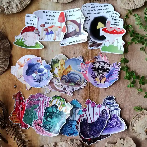 A collection of colorful, whimsical mushroom-themed stickers arranged on a wooden surface surrounded by natural elements…