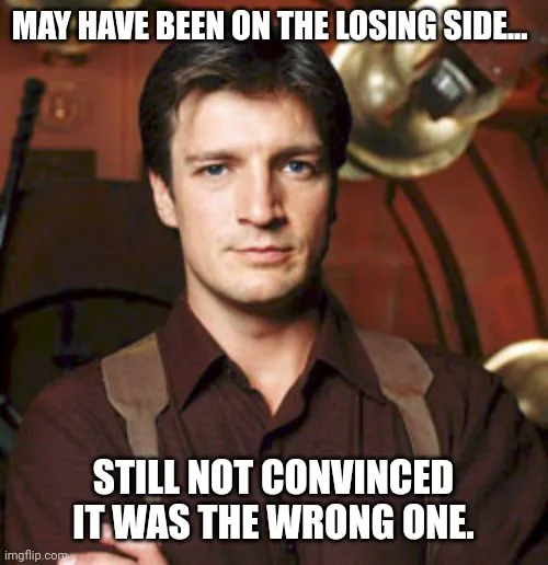 A man with a serious, slightly skeptical expression looks directly at the viewer. He wears a brown collared shirt with…