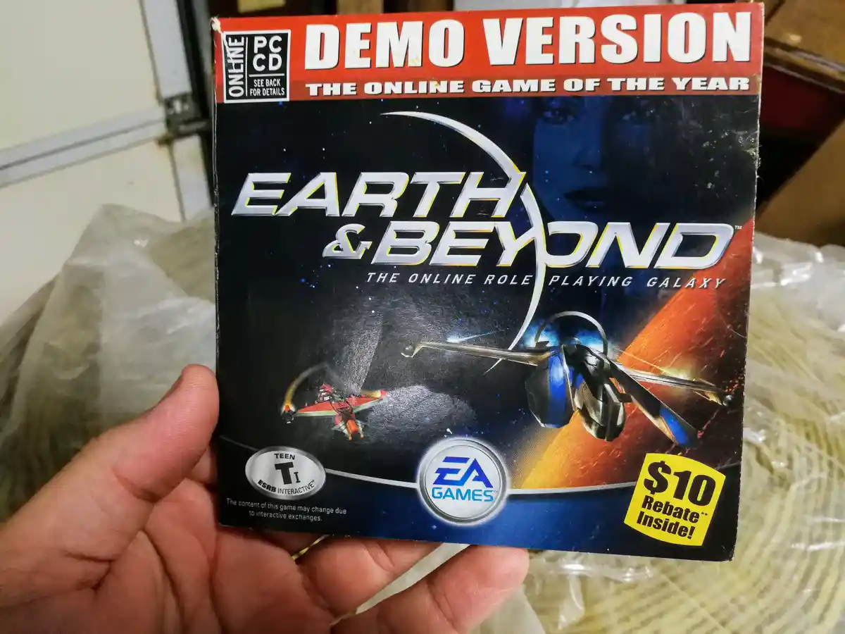 A hand holds a worn PC CD game case for 'Earth & Beyond: The Online Role Playing Galaxy' by EA Games, which prominently…