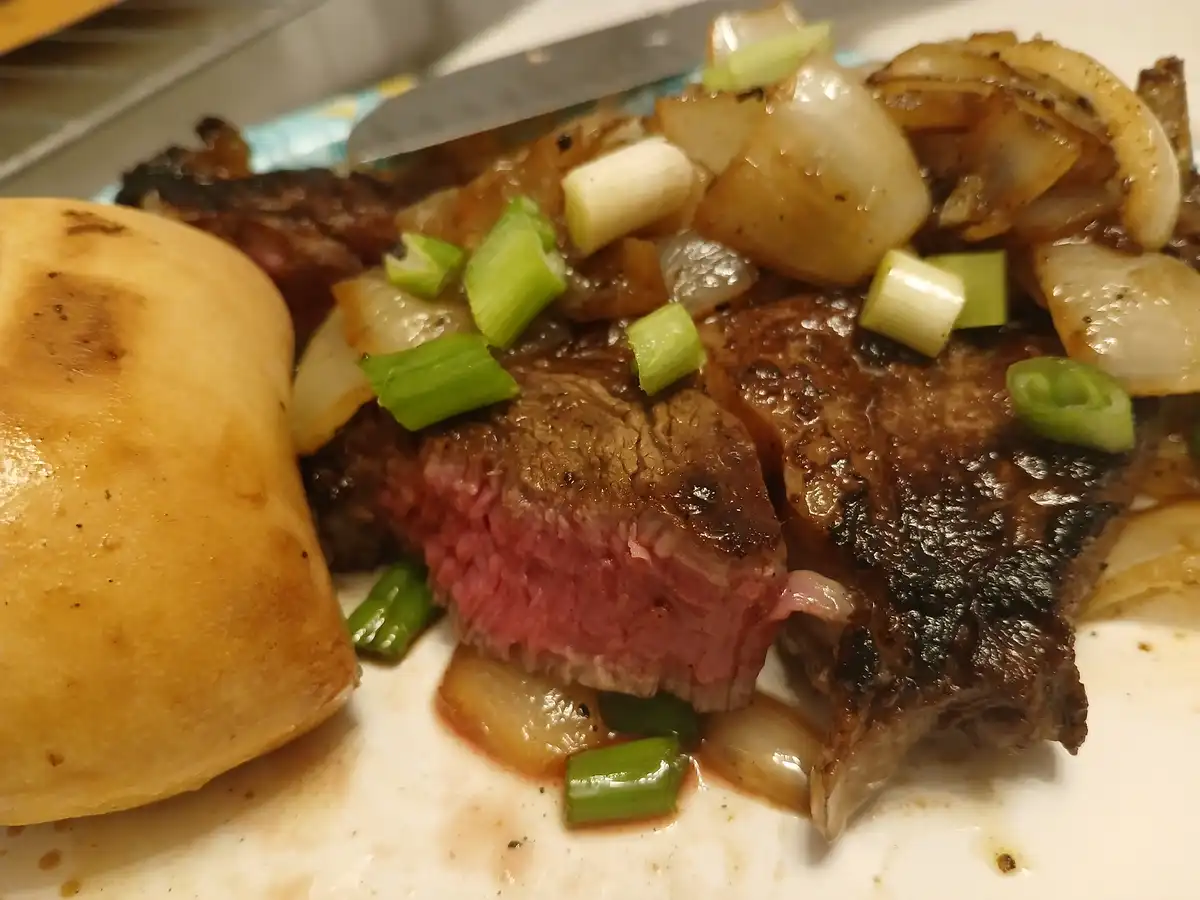 A close-up photo of a sliced steak on a plate, revealing a pink, rare center with a seared exterior, topped with caramelized…